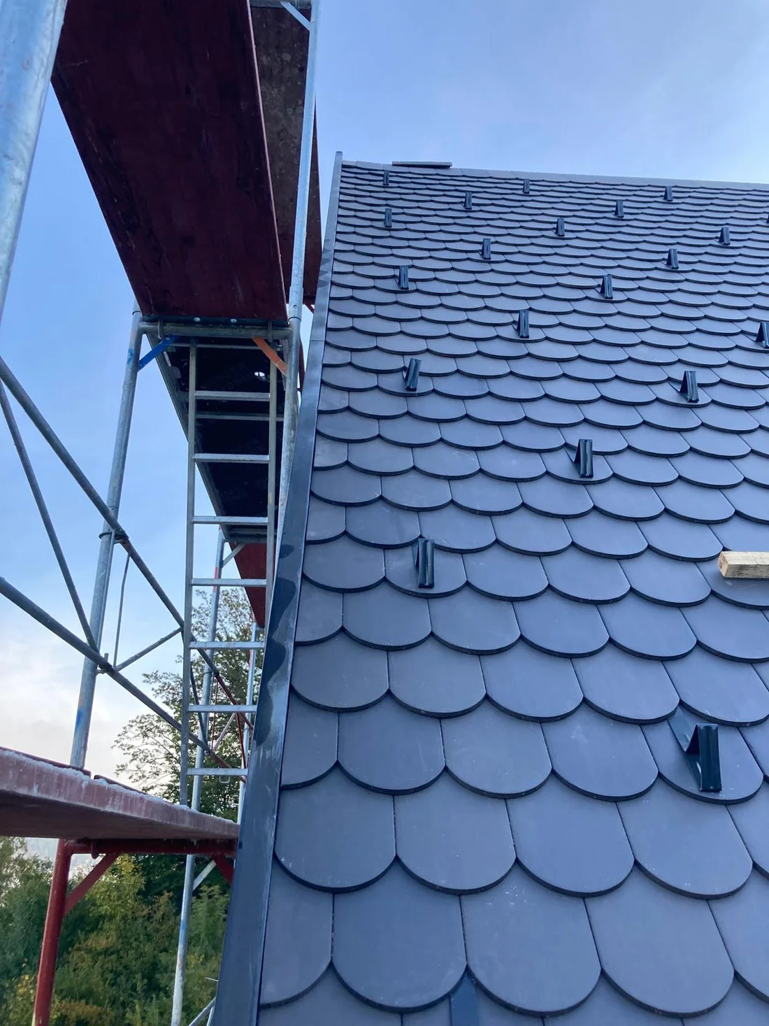 Steile Dachfläche mit dunkler Rundschnittdeckung und Schneefangelementen neben dem Gerüst