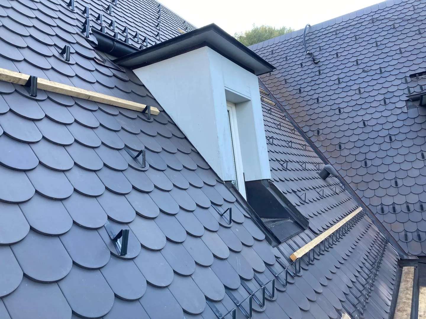 Dunkle Rundschnittdeckung mit heller Gaube und Metalleinfassungen am Wohnhausdach